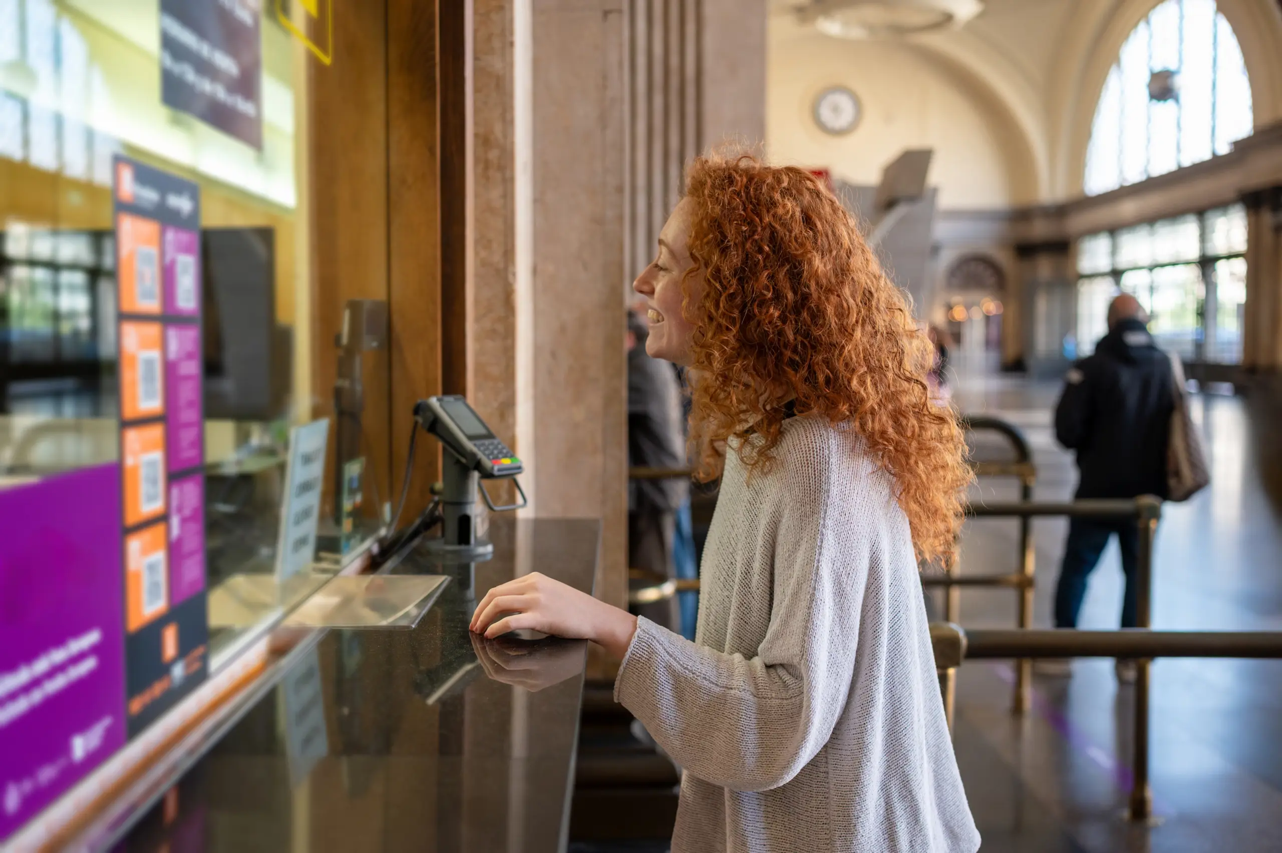 Frau kauft ein Ticket am Schalter und schaut auf die Anzeige. - Deutsch Marketing