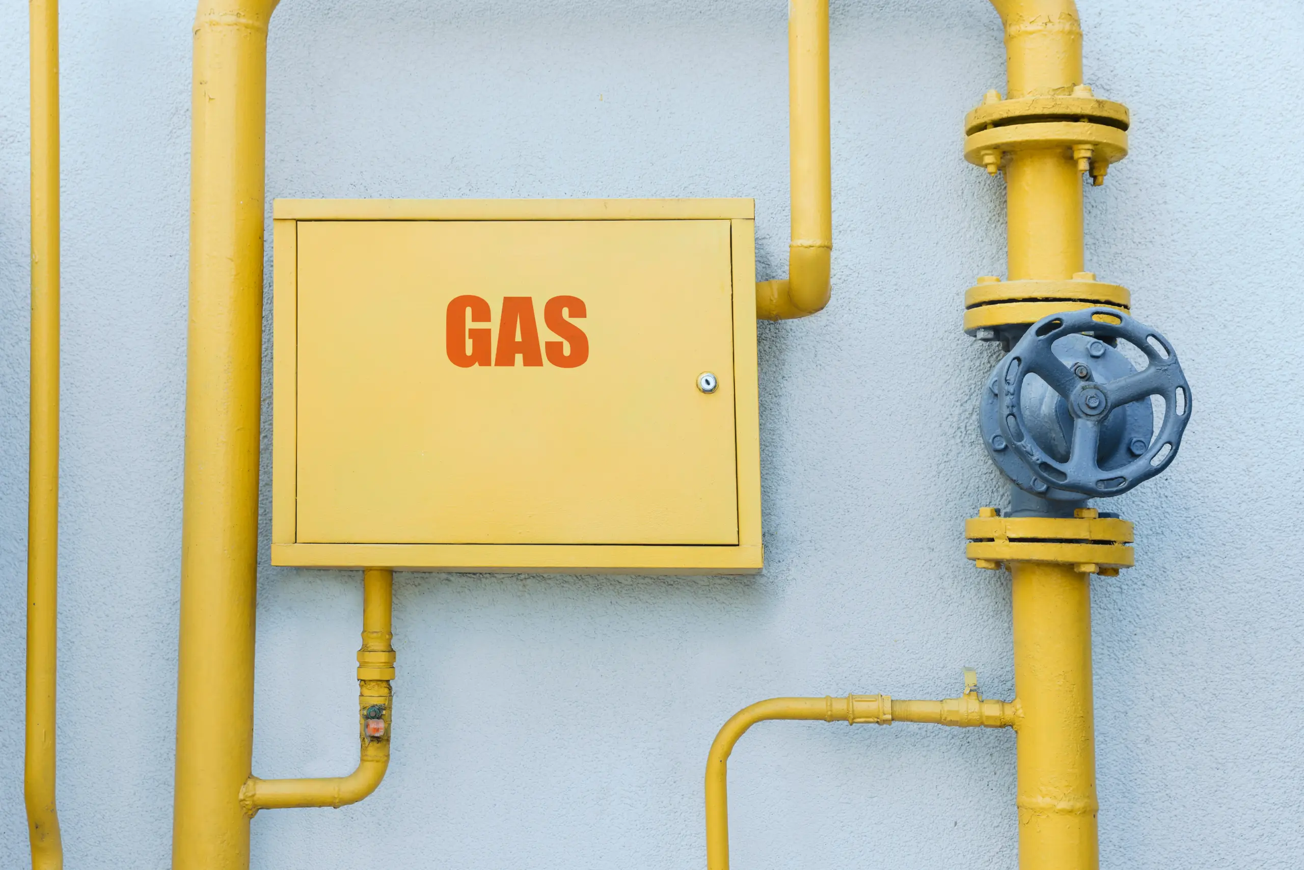 Gelbe Gasleitung mit Ventil und Gasanschlusskasten an Hauswand. - Deutsch Marketing GmbH